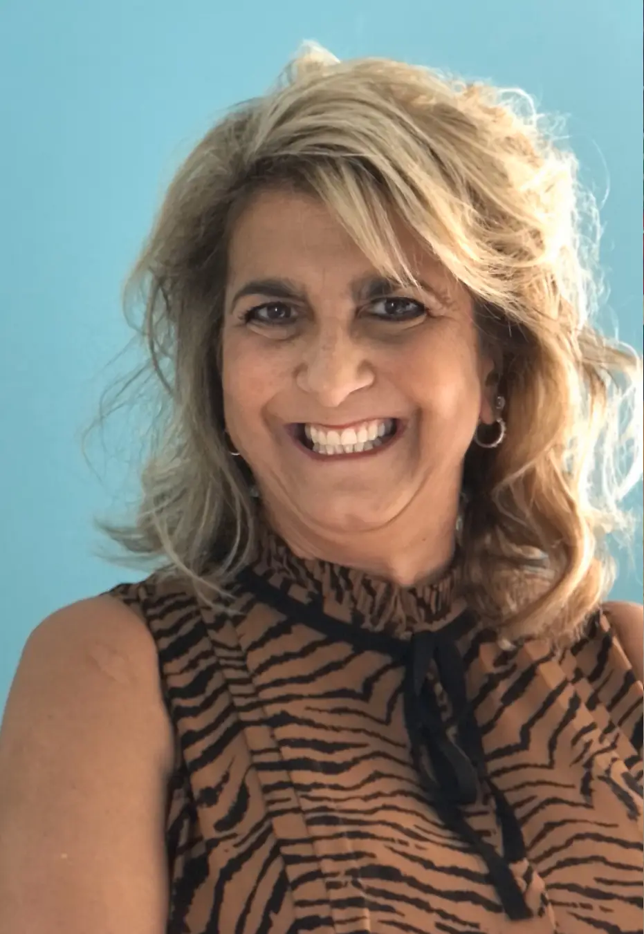 Smiling woman with blonde hair and a zebra-print top against a turquoise background.