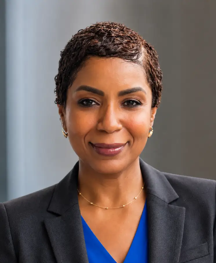 Professional woman with short curly hair in a blue blouse and black blazer, smiling at the camera.